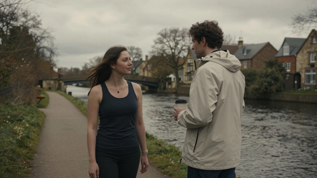 Two people by the river in York, one shivering without a jacket, another comfortable in a windbreaker under cloudy skies.